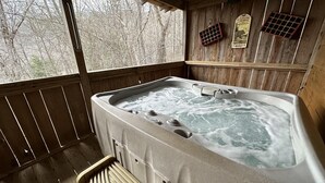 Eine Holzhütte mit Whirlpool, einer Holzterrasse und Blick auf Bäume.