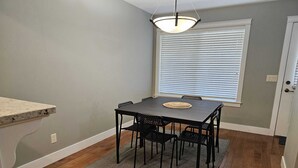 Un comedor con una mesa y sillas, un tapete, una ventana con persianas y una puerta.