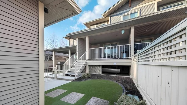 Un edificio residencial moderno de dos pisos con un porche cubierto, un césped pequeño y un patio cercado.