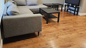 Una sala de estar con un sofá gris, dos mesas de centro negras y un televisor sobre un mueble.