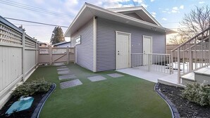 Una casa moderna con un patio cubierto, un jardín trasero cercado y un césped bien cuidado.