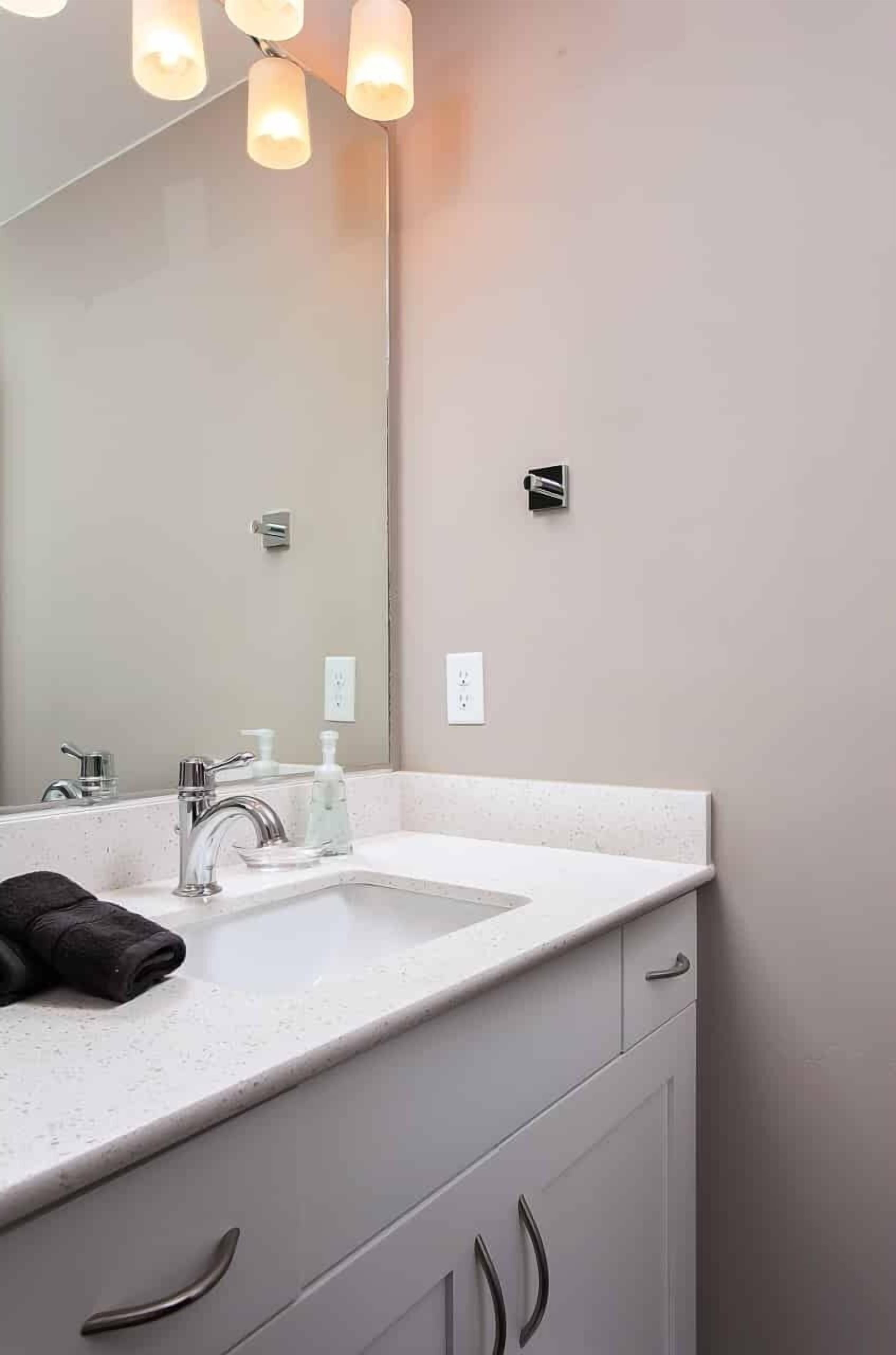 A bathroom with a white countertop, a large mirror, a modern faucet, and a towel on the sink.