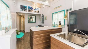Eine moderne Küche mit einer großen Kochinsel, Spüle aus Edelstahl und Holzschränken. Es gibt einen Deckenventilator, Kunstwerke an den Wänden und ein Fenster mit Vorhängen.