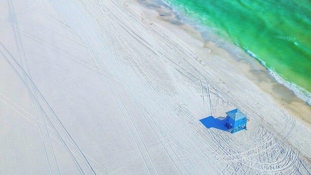 Ein Strand mit klarem türkisblauem Wasser, einem Sandstrand und einigen Strandsonnenschirmen.