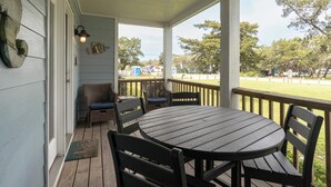 Eine überdachte Veranda mit rundem Tisch und vier Stühlen, einem Deckenventilator und Blick auf eine Wiese mit Bäumen.