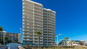 Un hotel de gran altura con varios balcones, una palmera y un cielo azul despejado.
