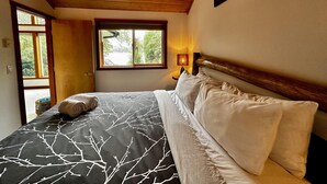 A bedroom with a bed, a window, a wooden ceiling, and a wall-mounted lamp.