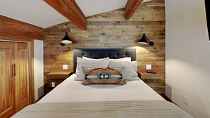 A bedroom with a wooden headboard, a bed with white bedding, two bedside tables, and a nightstand with a remote control.
