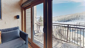 A balcony with a view of a snowy landscape, a blue sofa, and a metal chair.