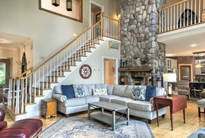 A spacious living room with a stone fireplace, a wooden staircase, and a large sectional sofa.