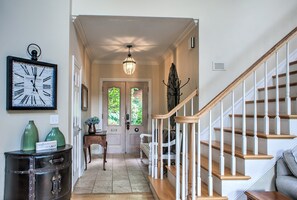 A hallway with a wooden staircase, a clock, and a door with glass panels.