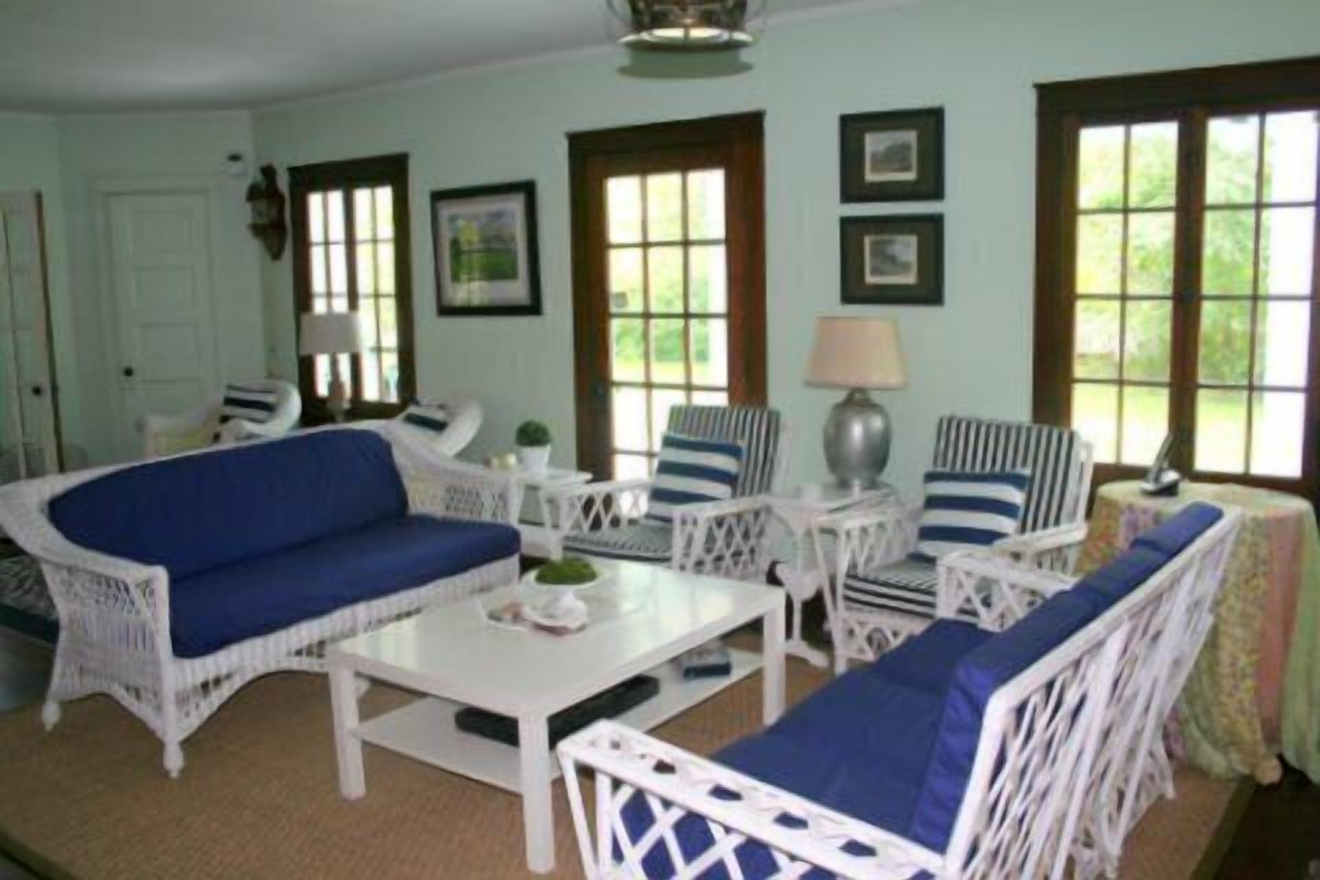 A room with a blue sofa, white wicker furniture, and large windows.