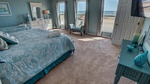 A bedroom with a bed, a dresser, a chair, and a door leading to a balcony with a view of the beach. - Pointe O'View | Oceanfront | Private Pool, Hot Tub (Virginia Beach)