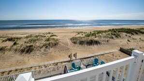 A beach view from a balcony with a wooden deck, featuring a sandy beach, dunes, and ocean. - Pointe O'View | Oceanfront | Private Pool, Hot Tub (Virginia Beach)
