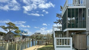 Une propriété située au bord de l’eau, dotée d’un quai, d’une terrasse en bois et d’une maison moderne avec de grandes fenêtres et un balcon.