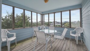 A covered patio with a round table and white chairs, large windows, and a view of houses and trees. - 1523 - Moby Vic's - Whalehead Retreat, 200 Yards to Corolla Beach (Corolla)