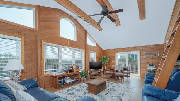 A spacious living room with a large TV, wooden furniture, and a ceiling fan. - 1523 - Moby Vic's - Whalehead Retreat, 200 Yards to Corolla Beach (Corolla)