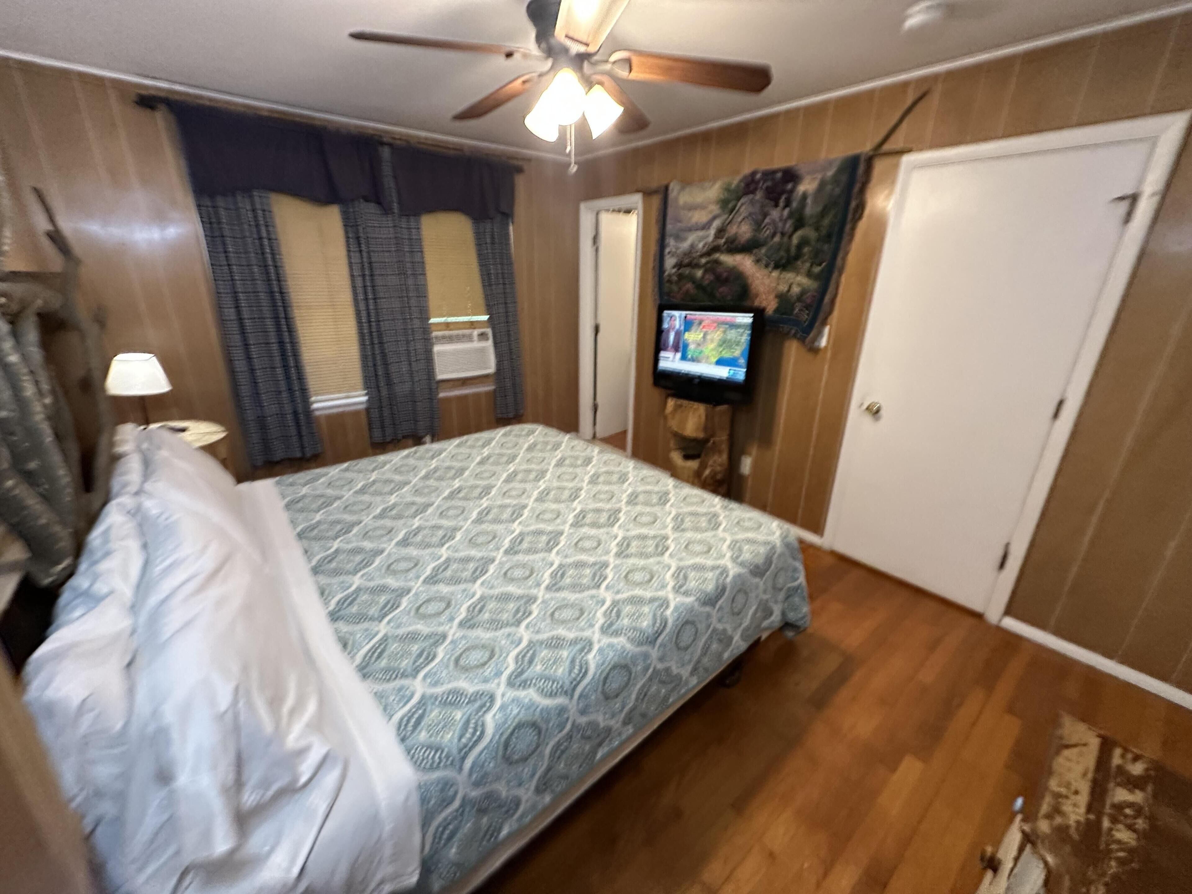 Een slaapkamer met een bed, een plafondventilator, een aan de muur bevestigde televisie en een deur.