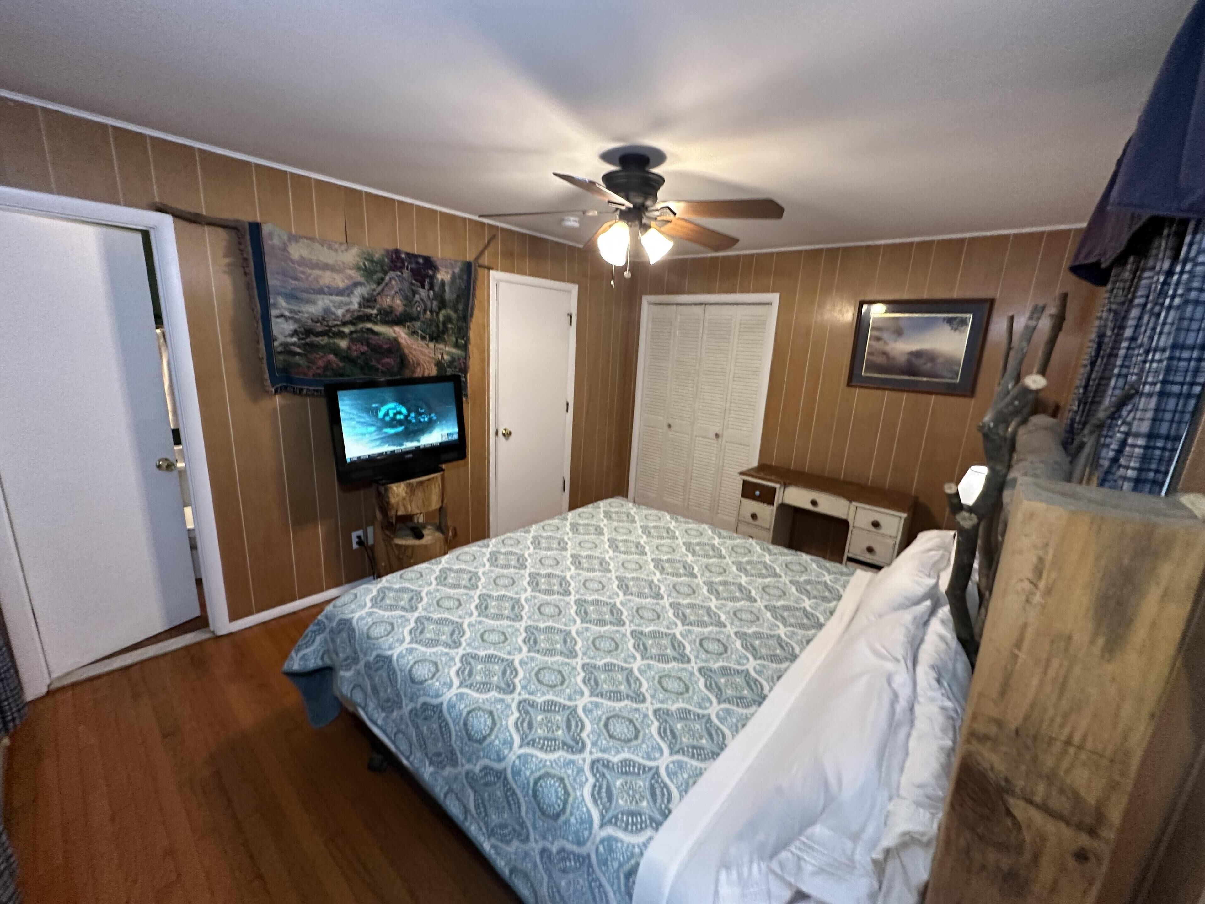 Un dormitorio con cama, ventilador de techo, televisor, puerta y cómoda.