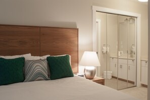 A hotel room with a wooden headboard, a bed with green and striped pillows, a bedside lamp, and a walk-in closet with a mirror.
