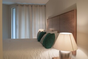 A hotel room with a bed, a nightstand with a lamp, and a large window with curtains.