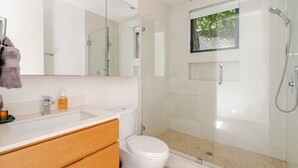 A modern bathroom with a glass-enclosed shower, a white toilet, and a vanity with a mirror and sink. - Contemporary suite in Santa Monica with private entrance (Santa Monica)