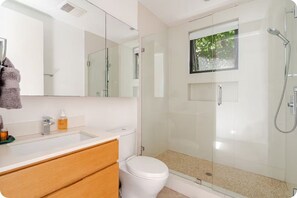 A modern bathroom with a glass-enclosed shower, a white toilet, and a vanity with a mirror and sink. - Contemporary suite in Santa Monica with private entrance (Santa Monica)