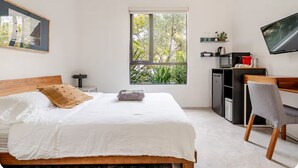 A bedroom with a bed, a desk, a chair, a television, a window with a view of trees, and a framed picture on the wall. - Contemporary suite in Santa Monica with private entrance (Santa Monica)