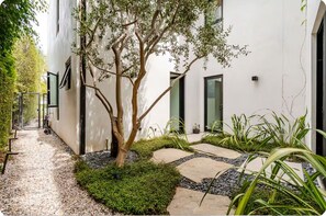 Um edifício moderno com um caminho, uma árvore e uma pequena área ajardinada.