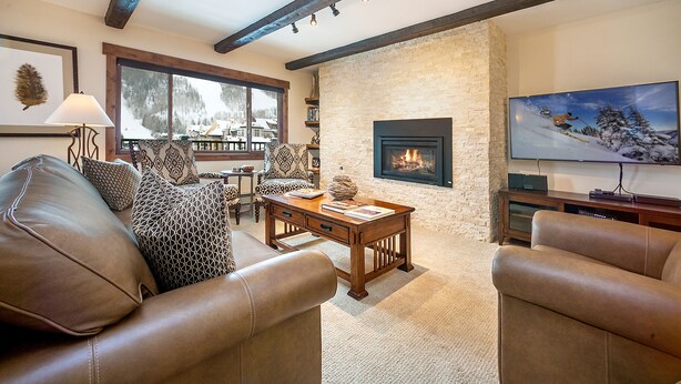 A cozy living room with leather sofas, a fireplace, a large TV, and a view of a snowy landscape through the window. - 2 Bed / 2 Bath With Amazing Views Steps From Gondola (Vail)