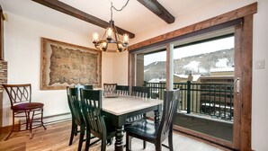 A dining area with a wooden table and chairs, a chandelier, and a large window with a view of a snowy landscape. - 2 Bed / 2 Bath With Amazing Views Steps From Gondola (Vail)