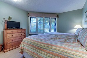 Ein Schlafzimmer mit einem Bett, einer Kommode, einem Fernseher darauf und einem Fenster mit Jalousien.