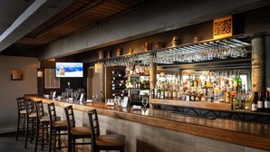 A bar area with a long counter, multiple bar stools, a television screen, and a variety of bottles and glasses. - 🌲Timberline B2D Deluxe 2-Bedroom ~Hot Tub~Pool~WiFi~Ski-in/out~Local Shuttle🌲 (Snowmass Village)