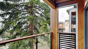 A balcony with a wooden railing, a view of a tree, and a building with a sign. - 🌲Timberline B2D Deluxe 2-Bedroom ~Hot Tub~Pool~WiFi~Ski-in/out~Local Shuttle🌲 (Snowmass Village)