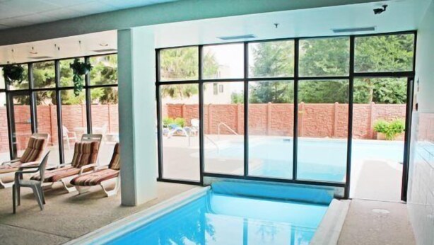 Una piscina interna con pareti di vetro trasparenti, una parete esterna in mattoni e sedie a sdraio.