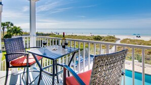 Un espacio al aire libre techado con una mesa y sillas, con vistas a una playa y una piscina.