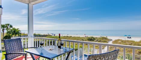 Un espacio al aire libre techado con una mesa y sillas, con vistas a una playa y una piscina.