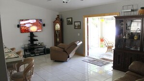 Una sala de estar con televisión de pantalla plana, un sillón reclinable, una zona de comedor con sillas, un mueble de madera y una puerta que da al exterior.