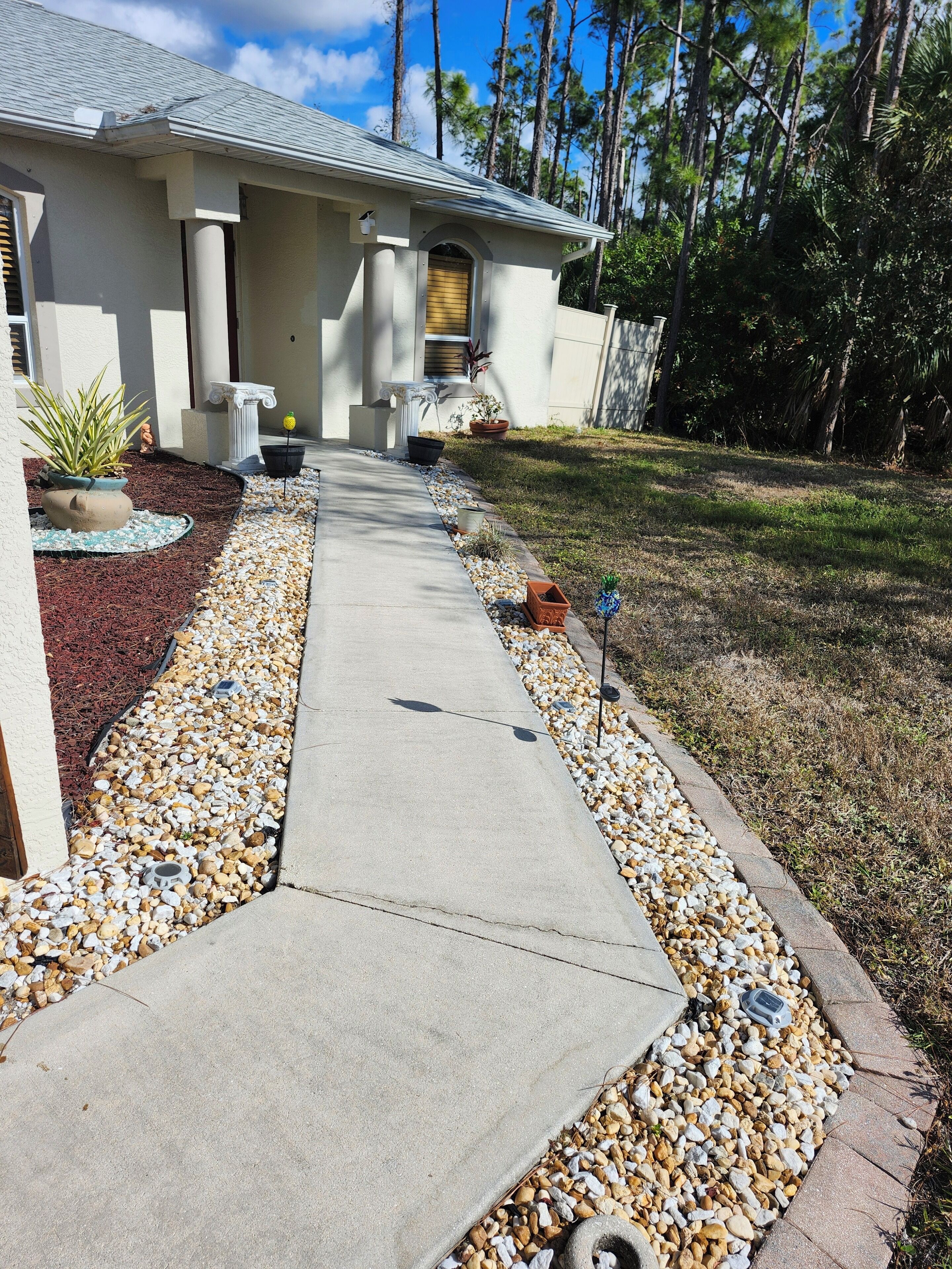 A house with a concrete pathway leading to the entrance, surrounded by a gravel border and small plants.