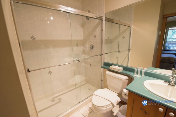 A bathroom with a glass-enclosed shower, a white toilet, a sink with a mirror, and a window providing natural light.