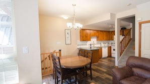 A modern kitchen with wooden cabinets, a dining area with a wooden table and chairs, a leather sofa, and a staircase leading to another level.