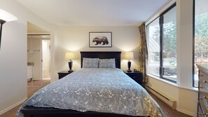 A bedroom with a bed, two bedside tables, a nightstand, a window with curtains, and a framed picture on the wall.
