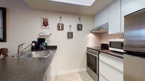 A modern kitchen with a stainless steel refrigerator, a built-in oven, and a microwave. There is a coffee maker on the counter, and the wall features decorative wooden letters and an owl painting. - Marquise on Blackcomb, Pool & Hot Tub, Easy Ski Access, Free WiFi (Whistler)
