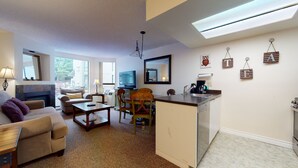 A living room with a sofa, coffee table, TV, and a fireplace. There is a kitchen area with a sink and a refrigerator. - Marquise on Blackcomb, Pool & Hot Tub, Easy Ski Access, Free WiFi (Whistler)