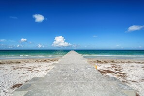 A concrete pathway leading to the beach with a clear blue sky and ocean in the background.