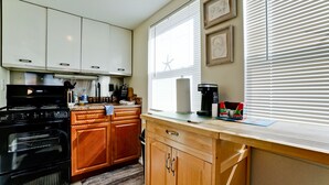 A kitchen with a stove, oven, wooden cabinets, a window with blinds, and a coffee maker.