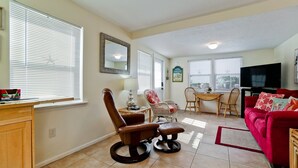 A living room with a red sofa, a wooden dining table with two chairs, a brown leather chair, and a television.