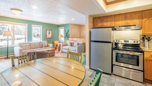 A modern kitchen with wooden cabinets, a stainless steel refrigerator, and an oven. There is a dining area with a round table and chairs.