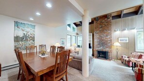 A dining area with a wooden table and chairs, a fireplace, and a living room with a sofa and armchairs.