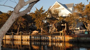A waterfront property with a white building, dock, and surrounding trees. - Aleta:  Pet friendly, waterfront, perfect for two. Private docking. (Ocracoke)